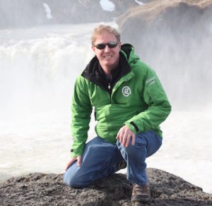 Jamie kneels in front of a waterfall.