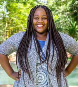 Evie Ndhlovu Rhea stands in front of water.